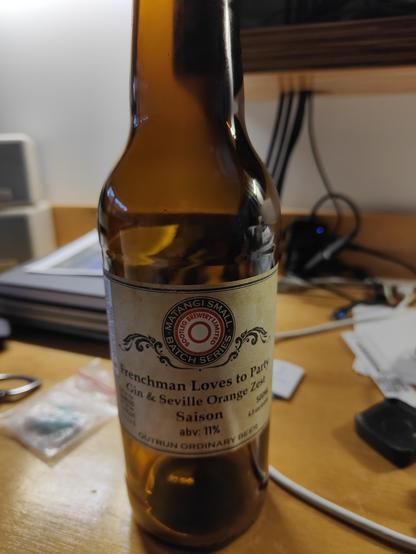 Photo of beer bottle on my desk. Label says "Frenchman Loves to Party" subtitle "Gone & Seville Orange Zest Saison" abv:11% from Bootleg Brewery. Yum. 