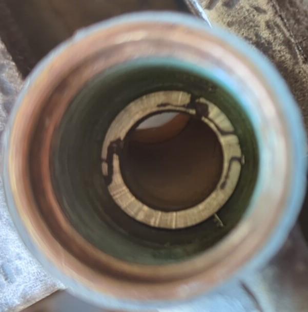 Part way through grinding. View of inside of tap body showing the bright brass circular valve seat with dark corrosion tracks across it.