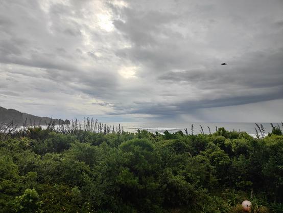 Sunset image to the west with ocean horizon and distant rocks to the left with lush green Aotearoa rain forest between our balcony and the sea and ominous dark grey rain cloud headed this way from the north west... 