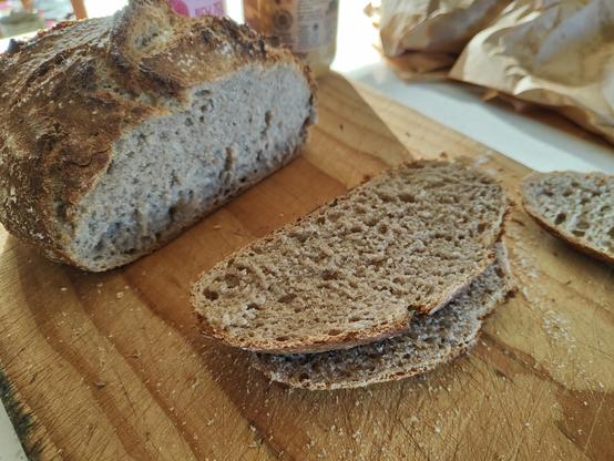A wooden cutting board with a couple slices of the bread and the remainder of the crusty round loaf showing the excellent crumb! 